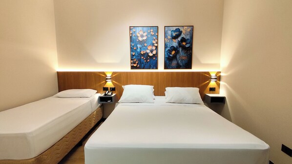 A hotel room with two single beds, a wooden headboard, bedside lamps, and two wall-mounted paintings. - SLAVIERO Londrina (Londrina)
