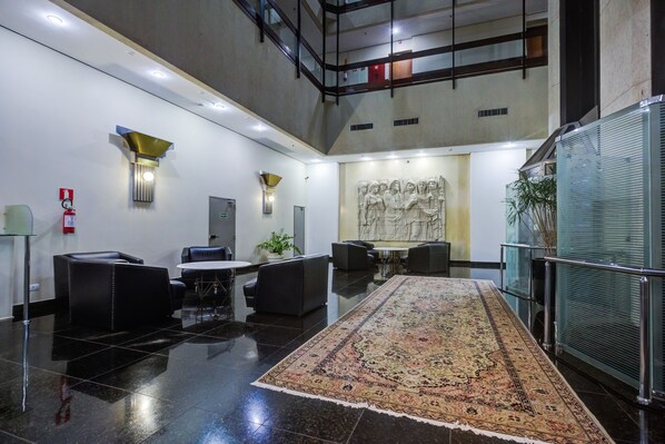A lobby with a black-tiled floor, a large patterned rug, a reception desk, and a wall-mounted sculpture. - SLAVIERO Londrina (Londrina)