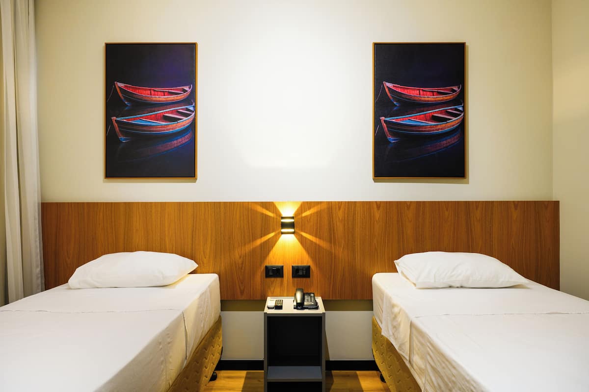 Une chambre d’hôtel avec deux lits, une table de chevet avec une lampe et deux tableaux représentant des bateaux accrochés au mur.