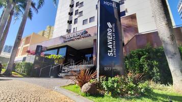 The Slavery Hotel entrance with a staircase leading up to the lobby, surrounded by palm trees and greenery.
