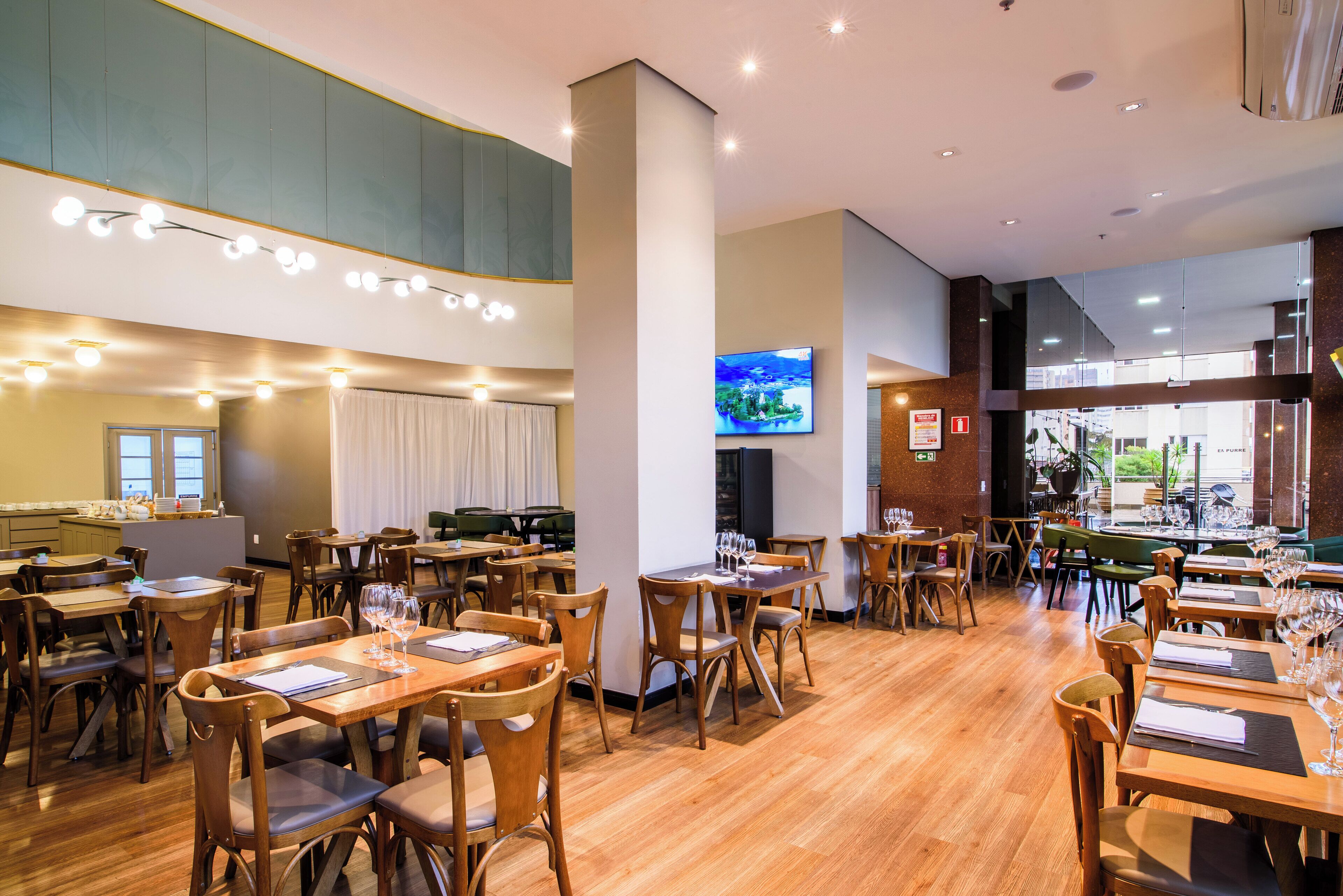 Un restaurante espacioso con mesas y sillas de madera, una gran pantalla de televisión y vista a la calle.