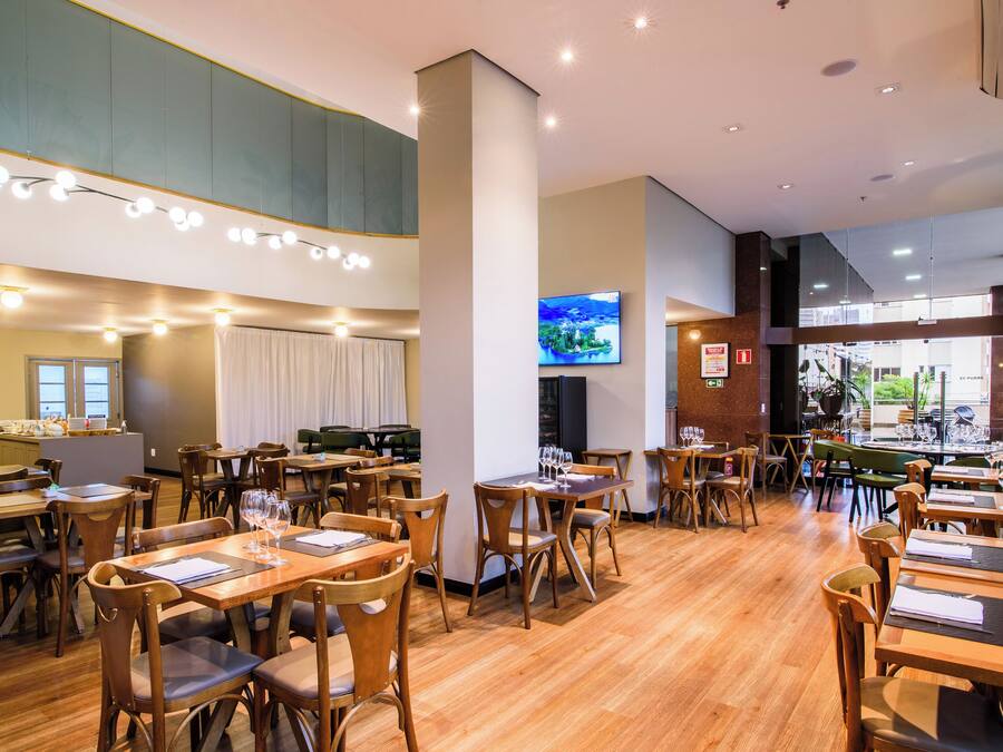 Un restaurante espacioso con mesas y sillas de madera, una gran pantalla de televisión y vista a la calle.