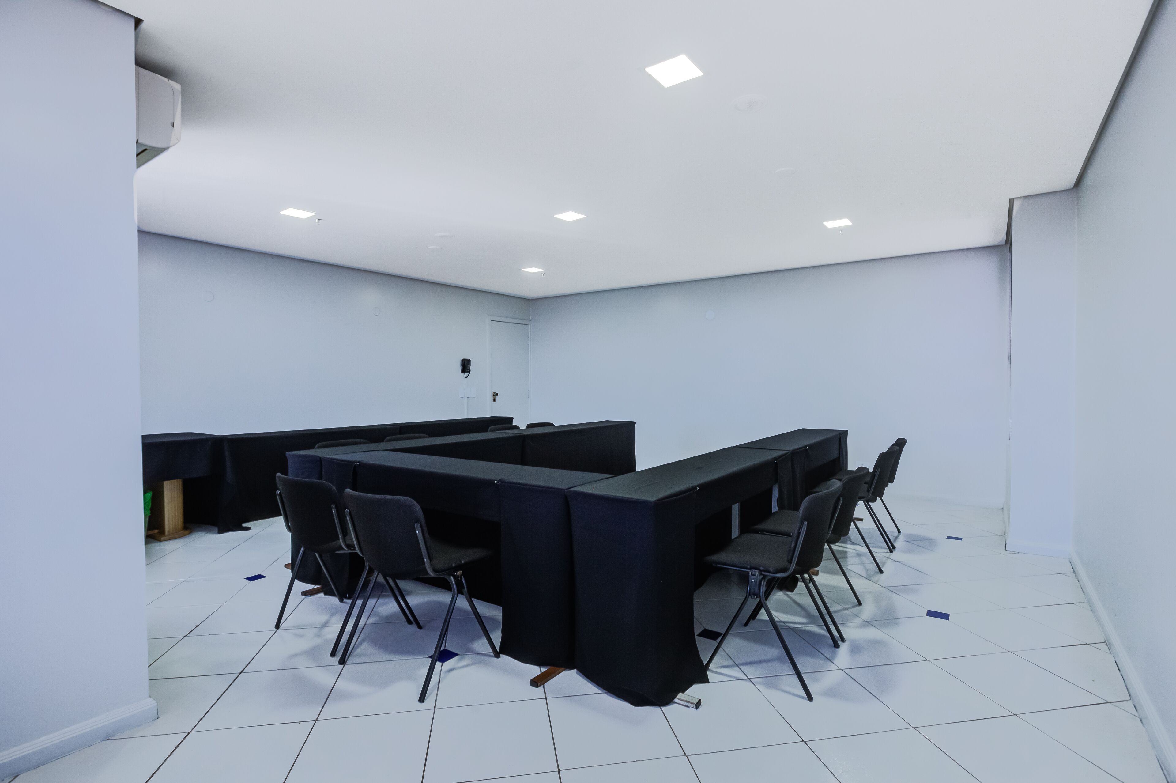 Uma sala de conferência com uma mesa comprida, cadeiras e teto branco com iluminação embutida.