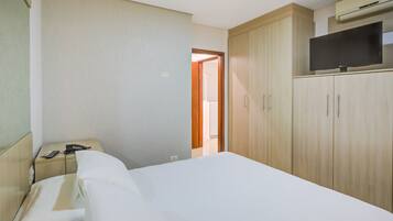 A hotel room with a bed, a desk with a telephone and a remote control, a wardrobe, and a television on top of the wardrobe.