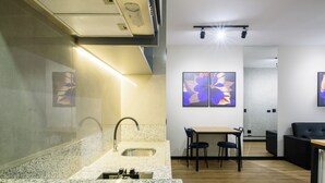 A modern bathroom with a granite countertop, a sink, and a mirror. There is a dining area with a table and chairs, and a black sofa. - SLAVIERO Londrina (Londrina)