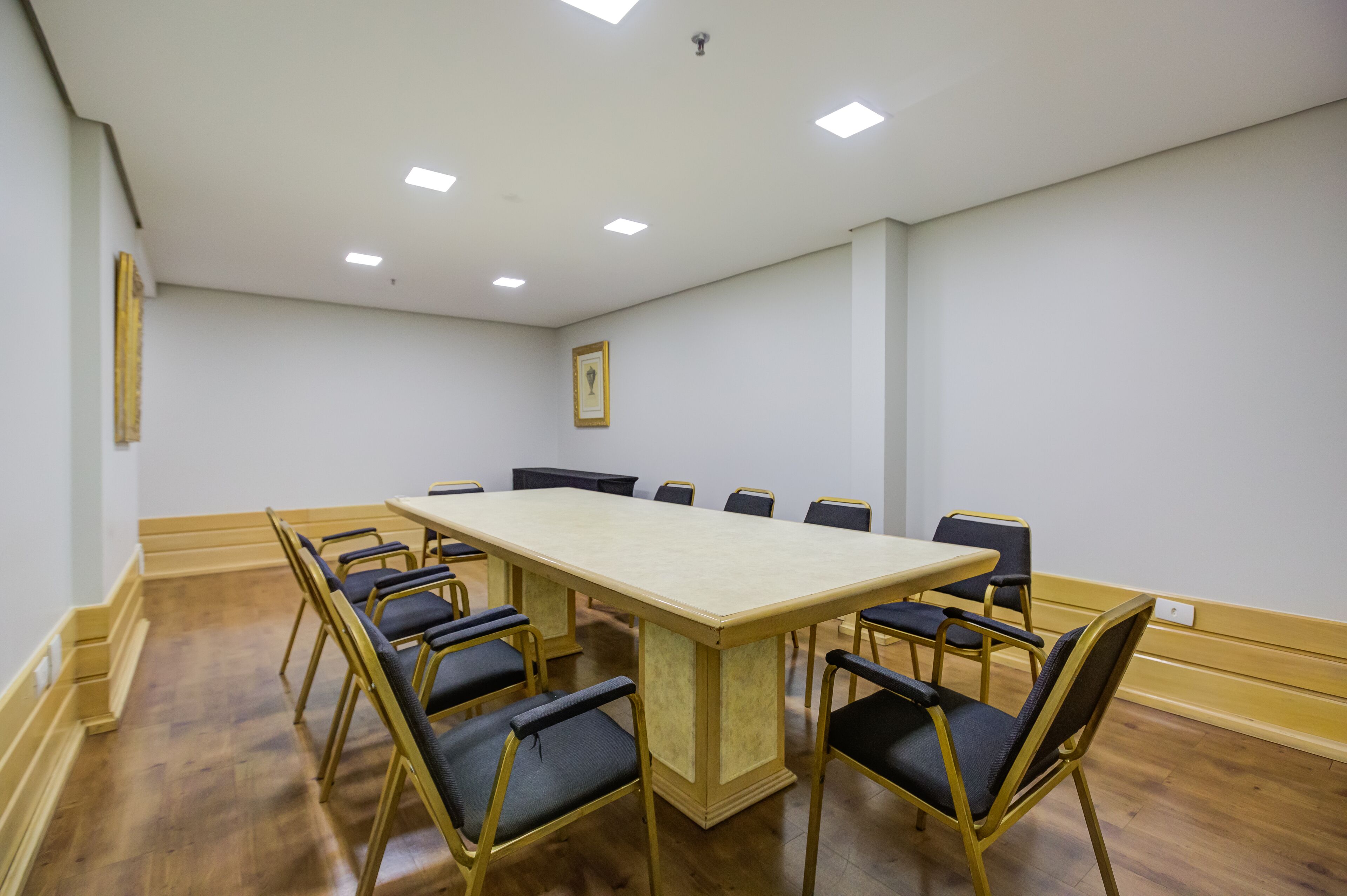 A conference room with a long table and chairs, white walls, and wooden flooring.