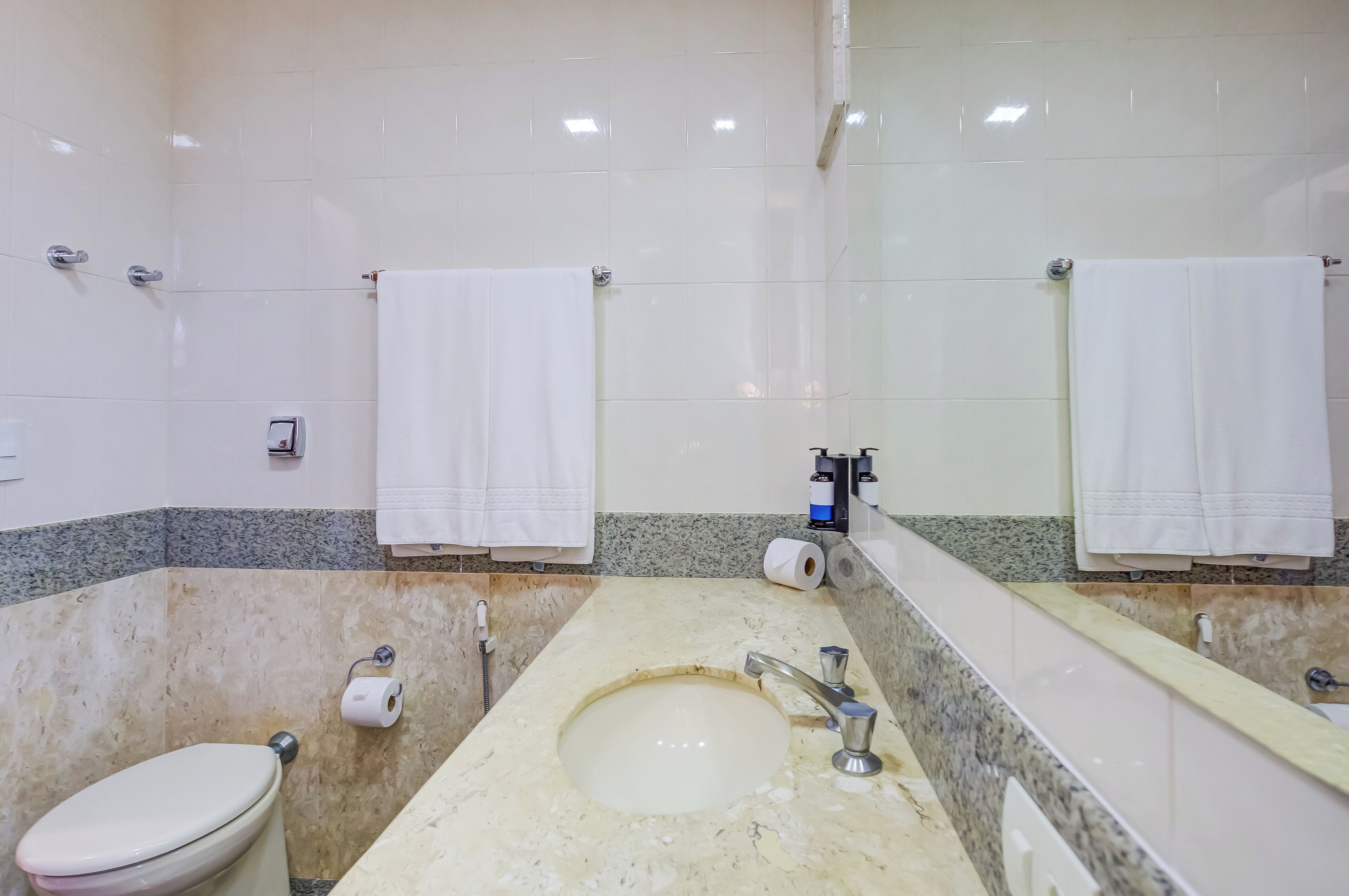 A bathroom with a white toilet, a sink with a mirror, and two towels hanging on towel racks.