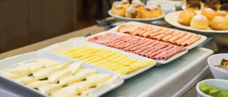 Un bufé con diferentes opciones de comida, incluyendo queso, jamón y pastelería.