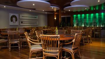 A restaurant with round tables and wicker chairs, featuring a modern ceiling design and a green-lit wall.