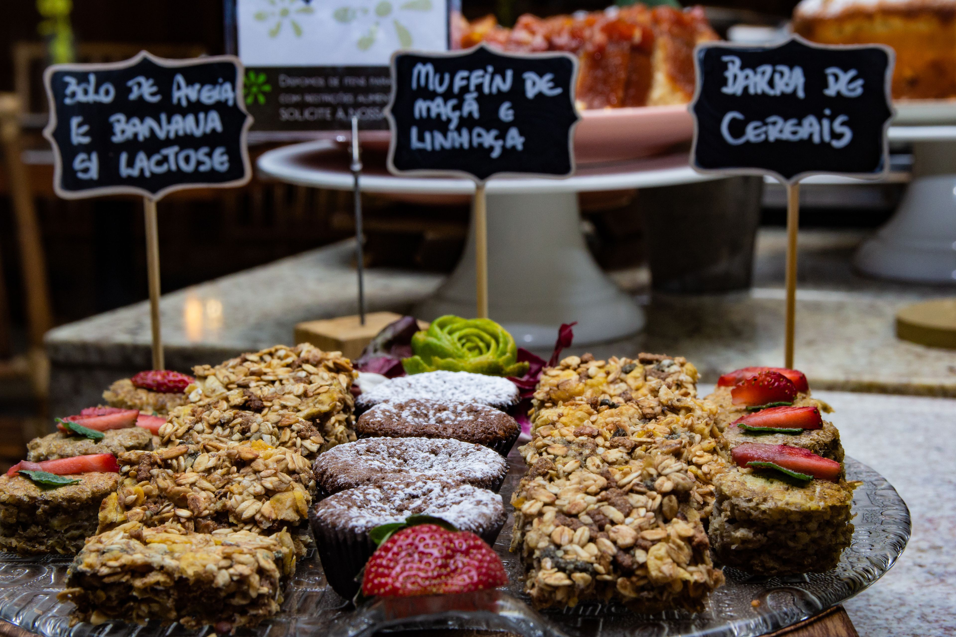 Une variété de produits de boulangerie présentés sur un plateau en verre, avec des étiquettes indiquant les différents types de muffins et de biscuits.
