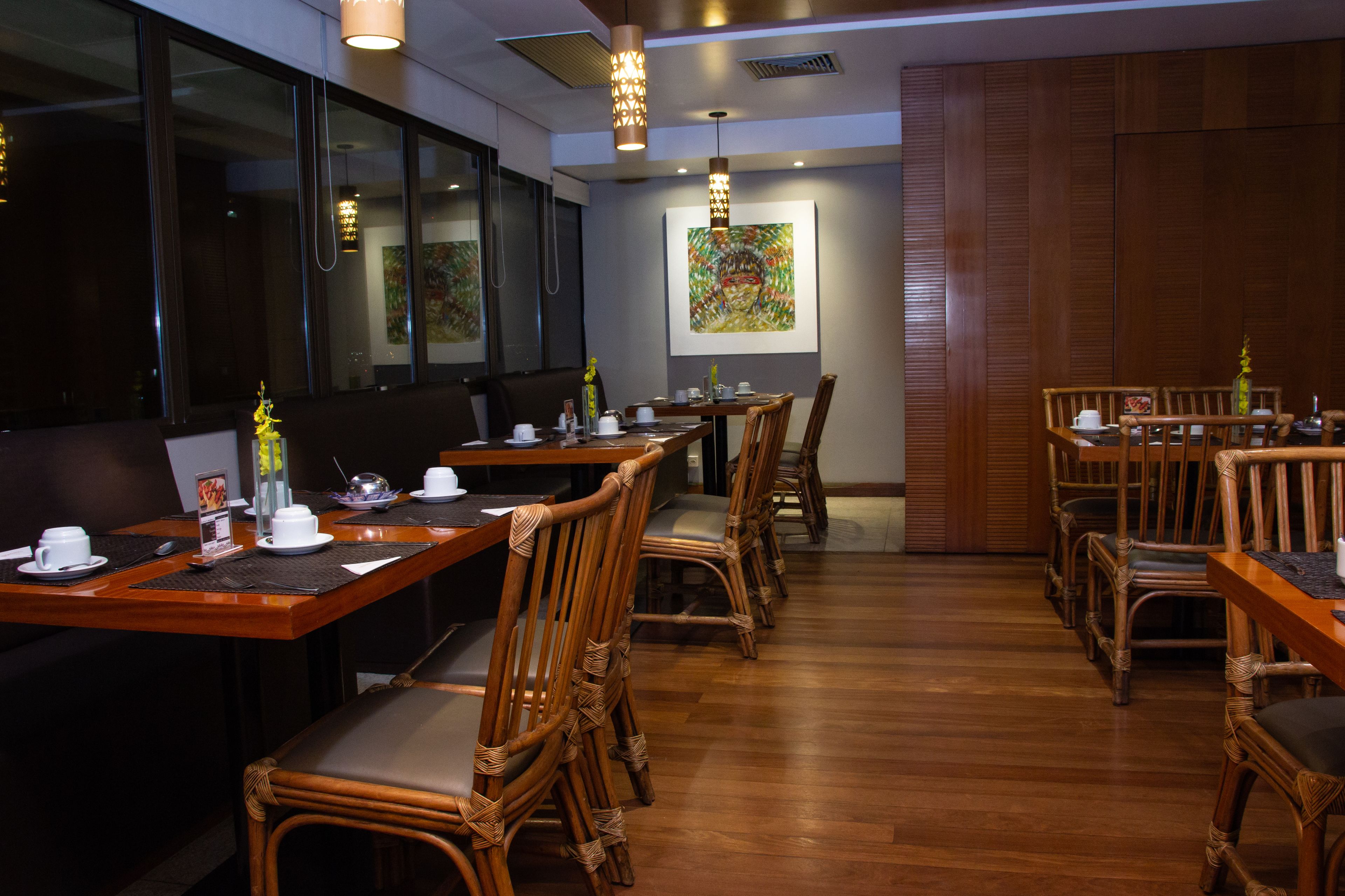 A restaurant with wooden tables and chairs, a large window, and a painting on the wall.