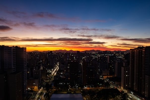 A cityscape at dusk with a sunset over the mountains, high-rise buildings, and illuminated streets.