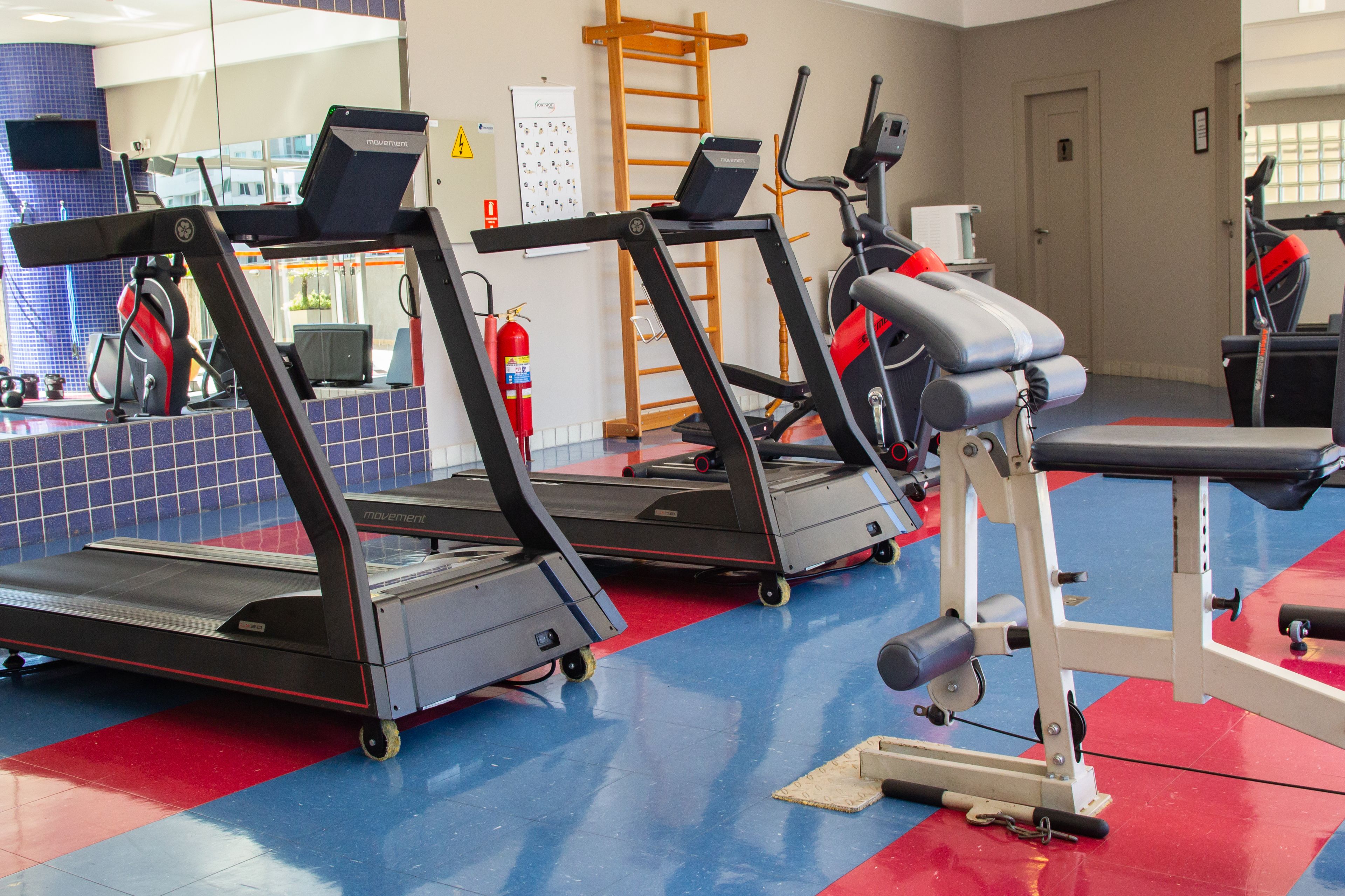 Een fitnessruimte met loopbanden, een hometrainer en een halterbank.