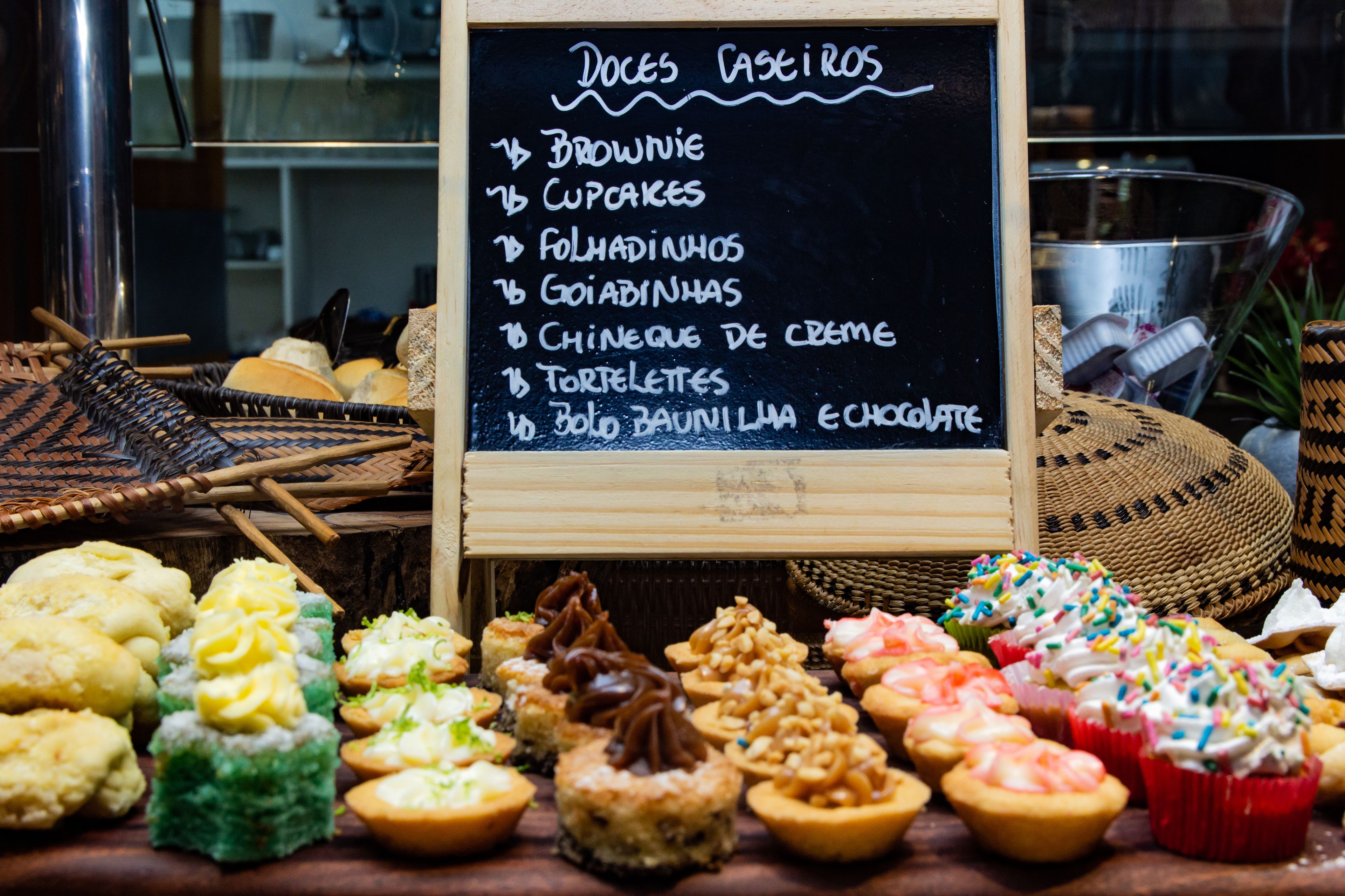 Diverse gebakjes uitgestald voor een krijtbord met een menu, waarop onder meer brownies, cupcakes en chocolade staan vermeld.