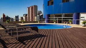 Zona de piscina en la azotea con cubierta de madera, sillas de descanso y plantas en macetas.