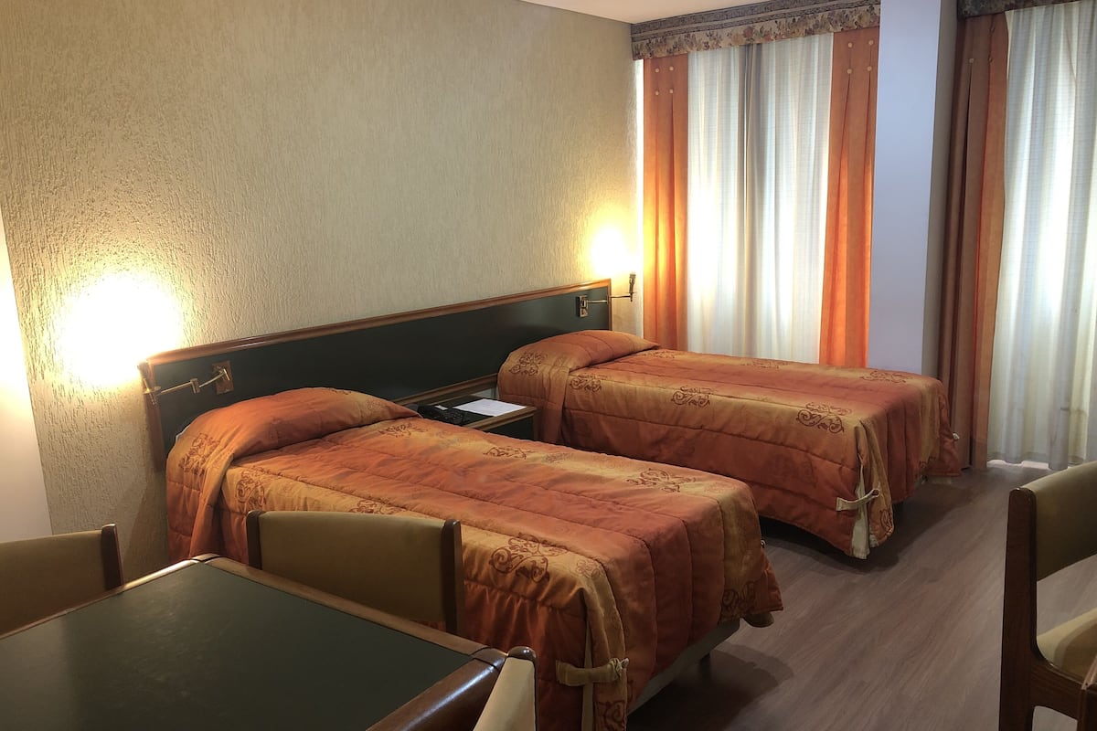 Habitación de hotel con dos camas, una mesita y una silla.