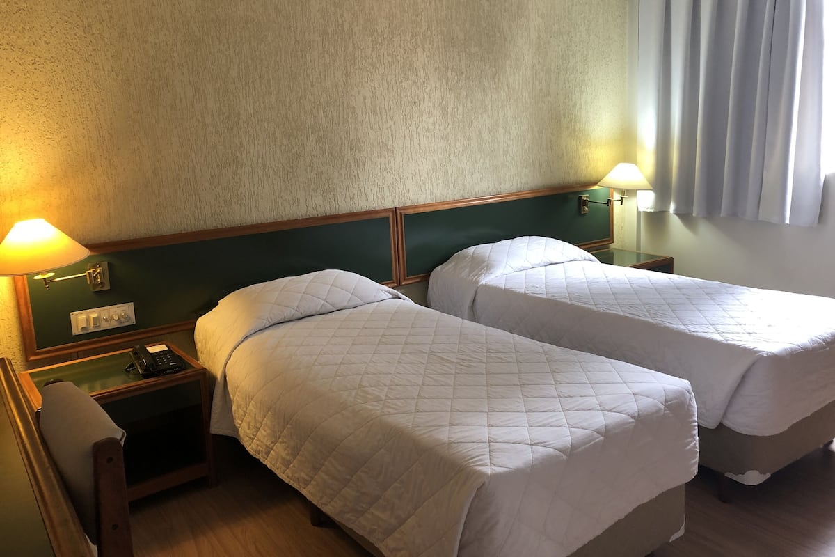Una habitación de hotel con dos camas individuales, una mesita de noche con teléfono y una lámpara.