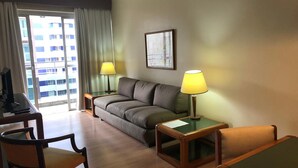 A hotel room with a sofa, two armchairs, a small table, a TV, and two lamps. - Duomo Park Hotel (Curitiba)