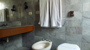 Un baño con pared de mármol, un lavamanos, un bidé y dos toallas colgadas en un perchero.