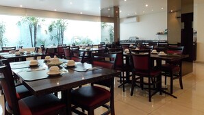 A restaurant with multiple tables and chairs, a kitchen area, and large windows with a view of palm trees. - Duomo Park Hotel (Curitiba)