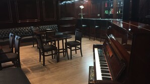 A dimly lit room with a piano, a bar area, and a seating area with a sofa and chairs. - Duomo Park Hotel (Curitiba)