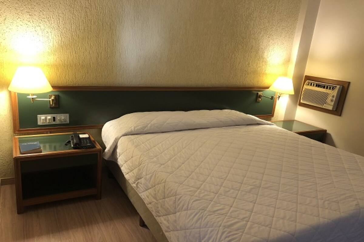 Habitación de hotel con cama, dos lámparas de noche, una mesita de noche con teléfono y un calentador de pared.