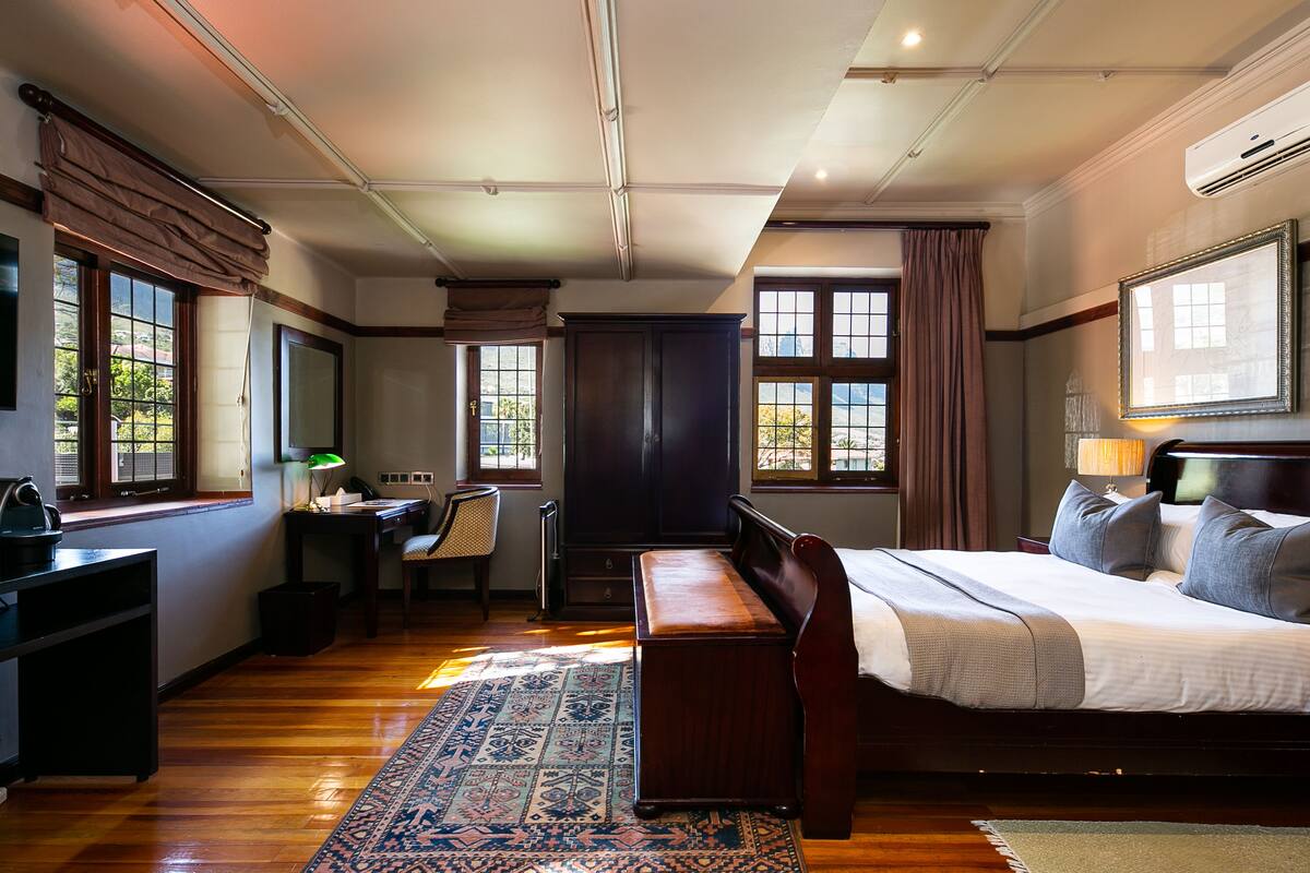 A hotel room with a large bed, a desk, a chair, and a wardrobe.