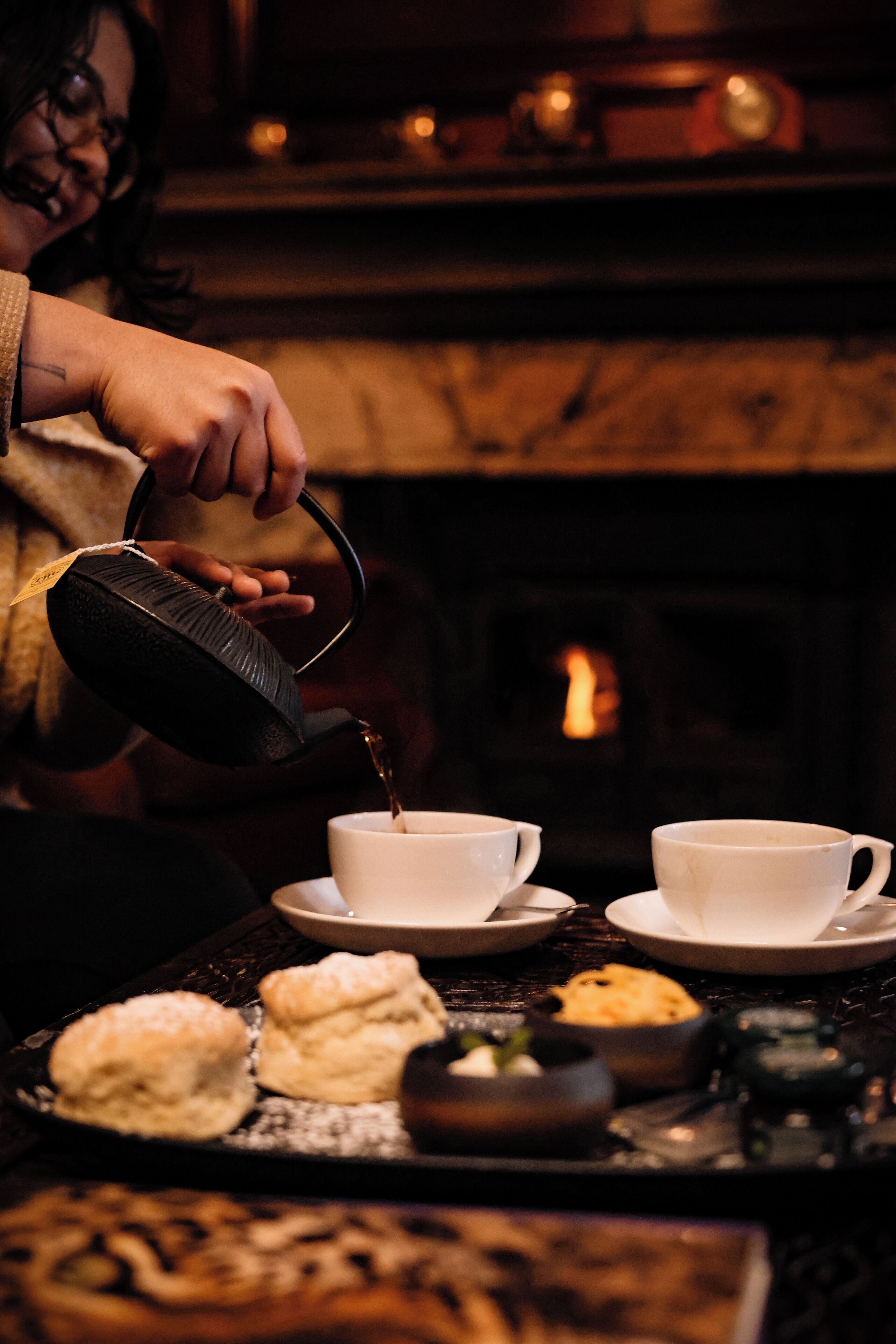 A person pouring tea into a cup, with a fireplace in the background.