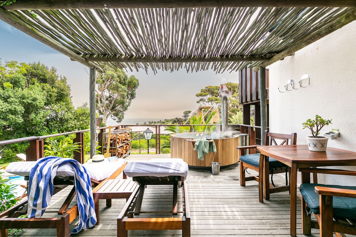 An outdoor deck with wooden furniture, a hot tub, and a pergola.