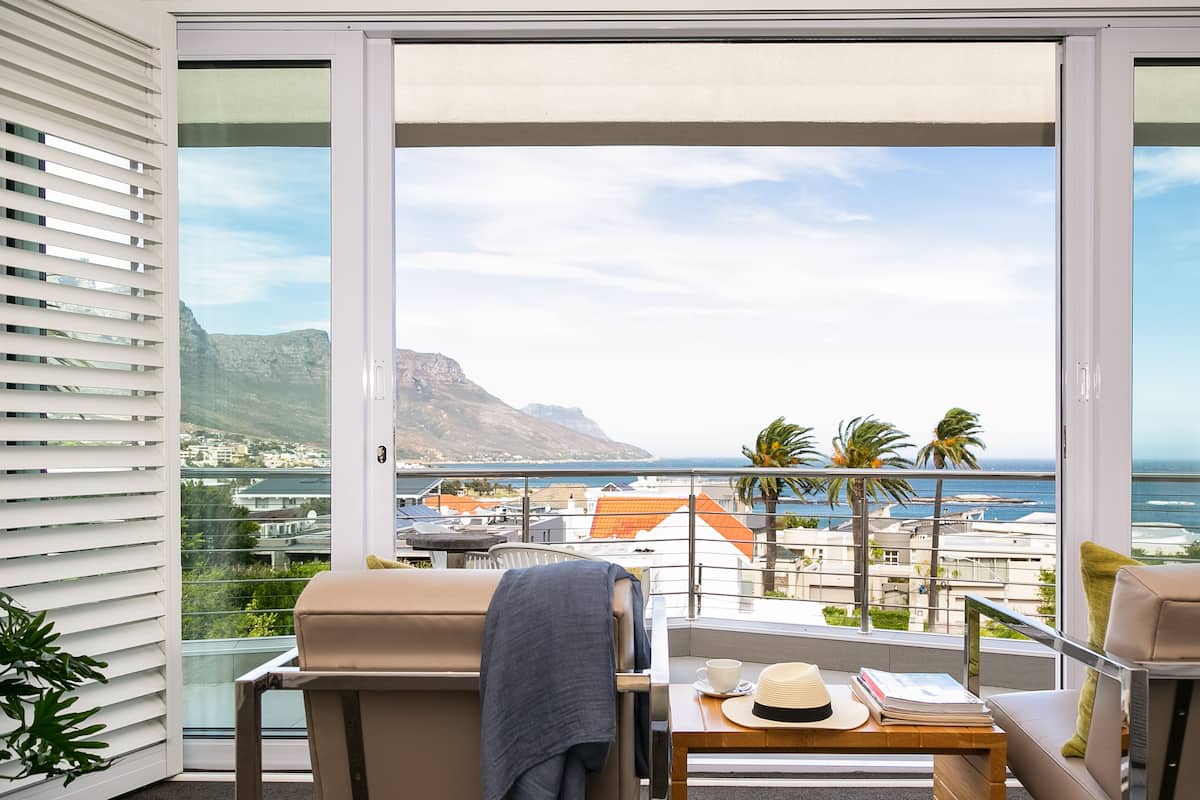 A balcony with a view of the sea, a table with a hat and a book, and a chair with a blanket.