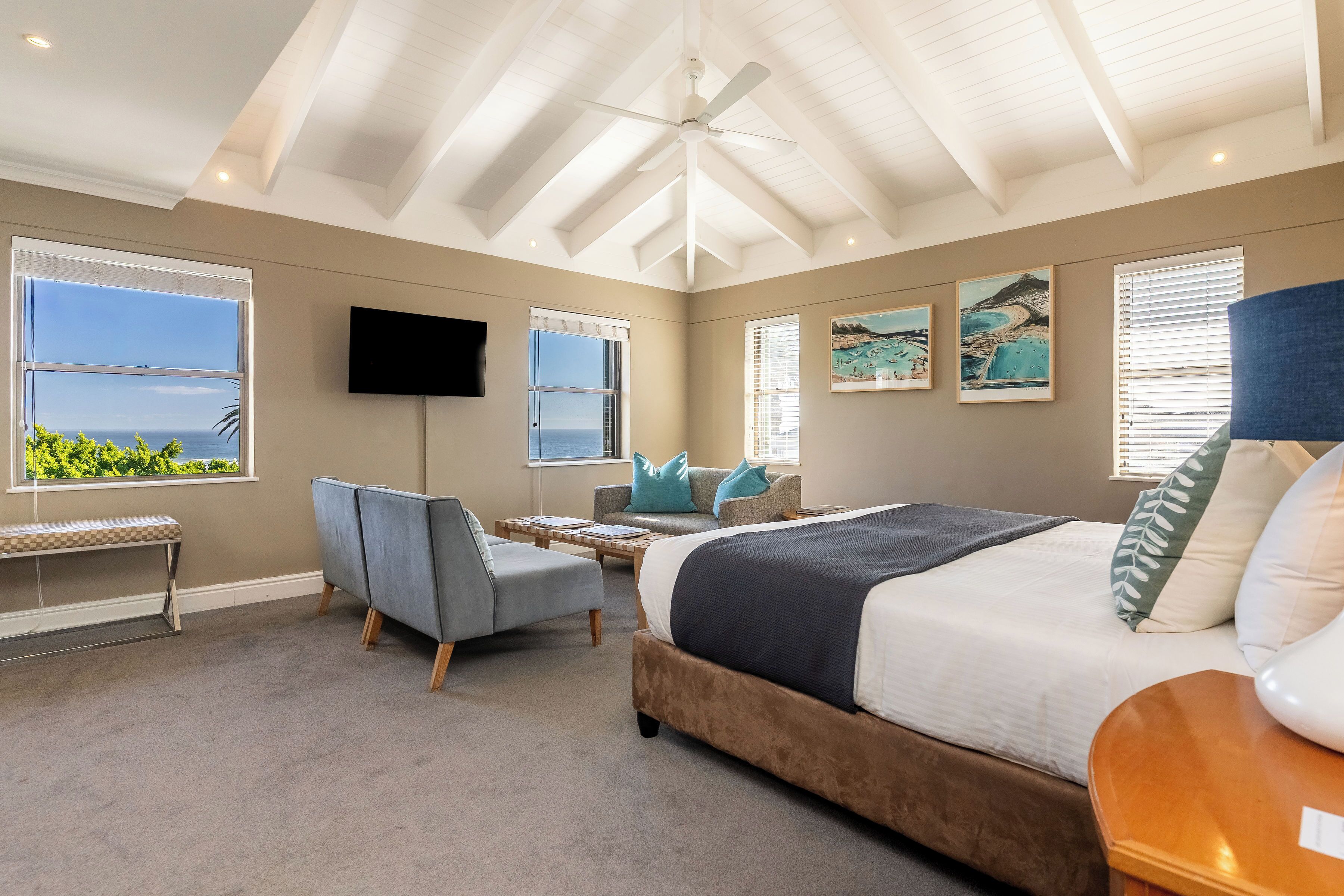 A bedroom with a bed, a desk, a chair, a bench, and a TV.