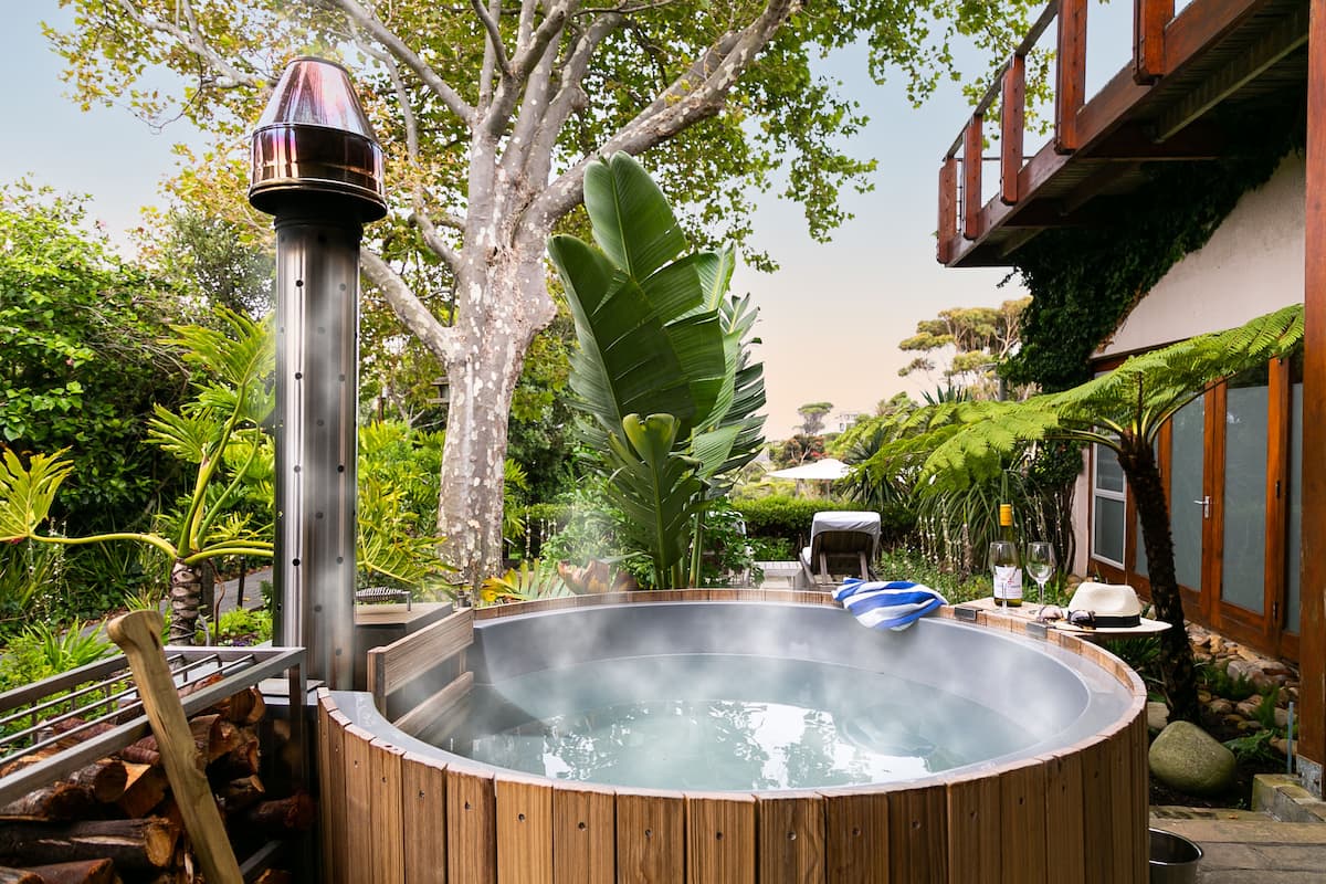 A hot tub surrounded by lush greenery, a wooden deck, and a stone wall.