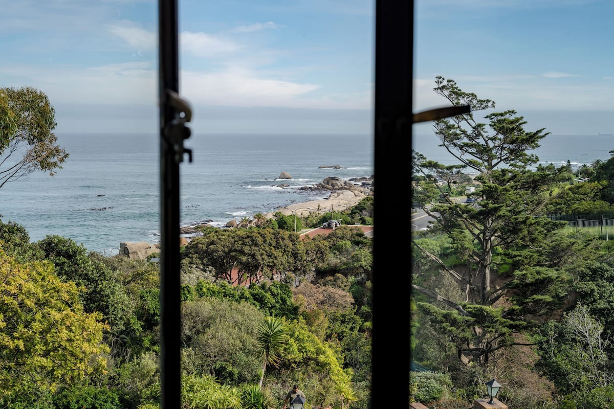 A coastal view through a window with a view of the ocean, rocky shoreline, and lush greenery.