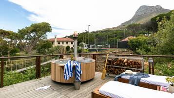 A wooden deck with a hot tub, a bed, and a view of a mountain.