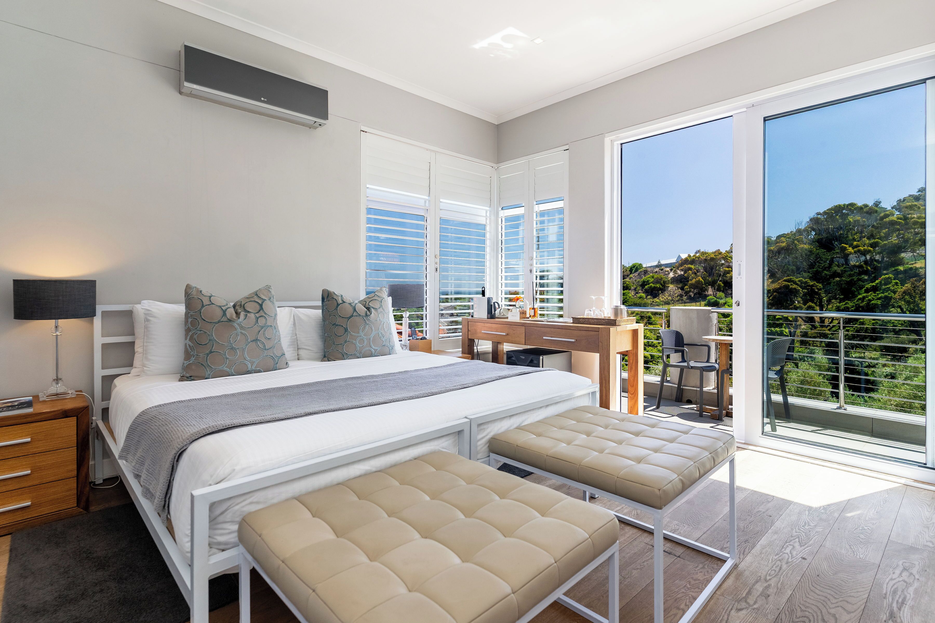 Ein modernes Schlafzimmer mit Bett, Nachttischen, einem Schreibtisch und einem Balkon mit Aussicht.