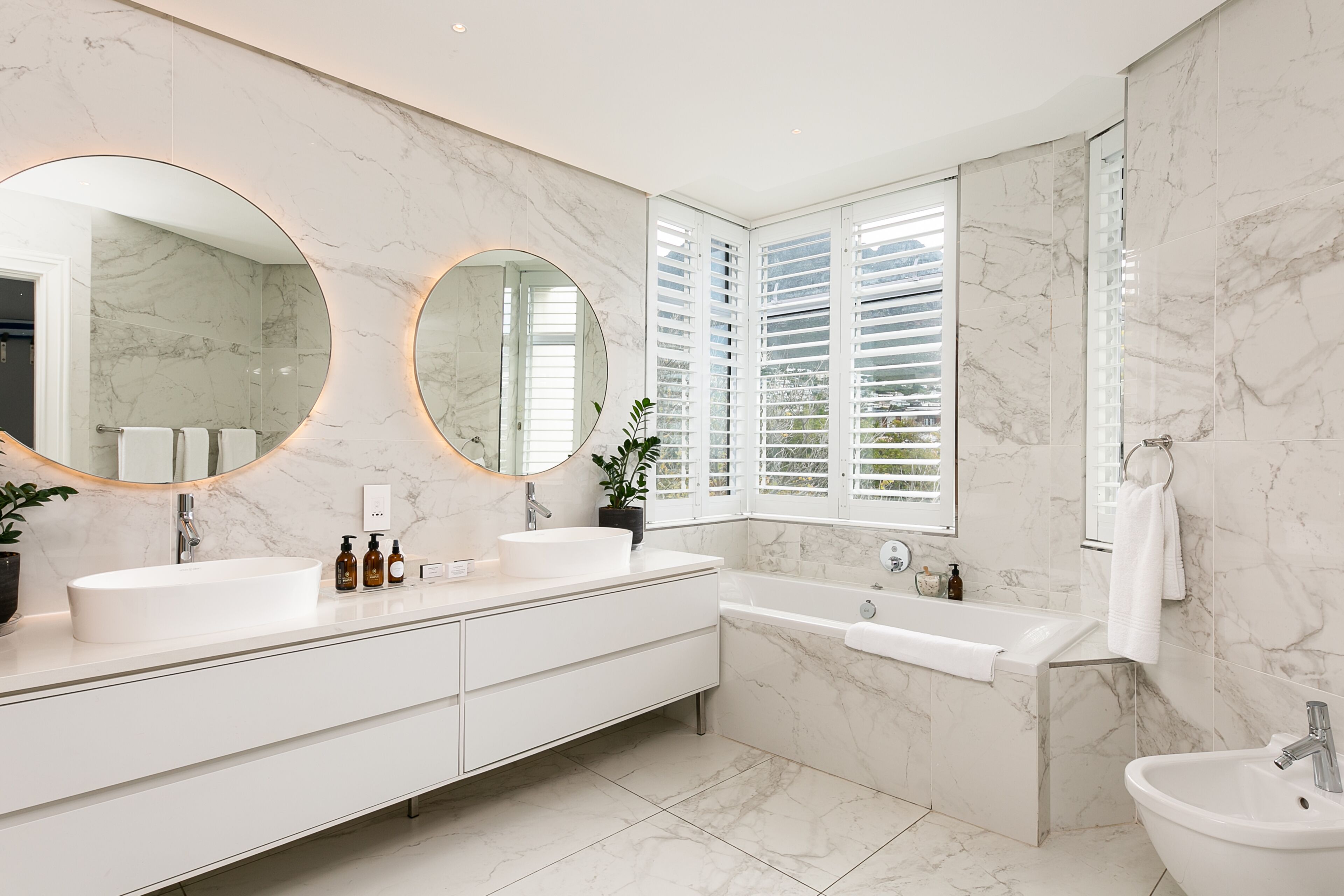 Une salle de bain moderne avec un grand miroir ovale, deux lavabos, une baignoire et un lavabo sur pied.