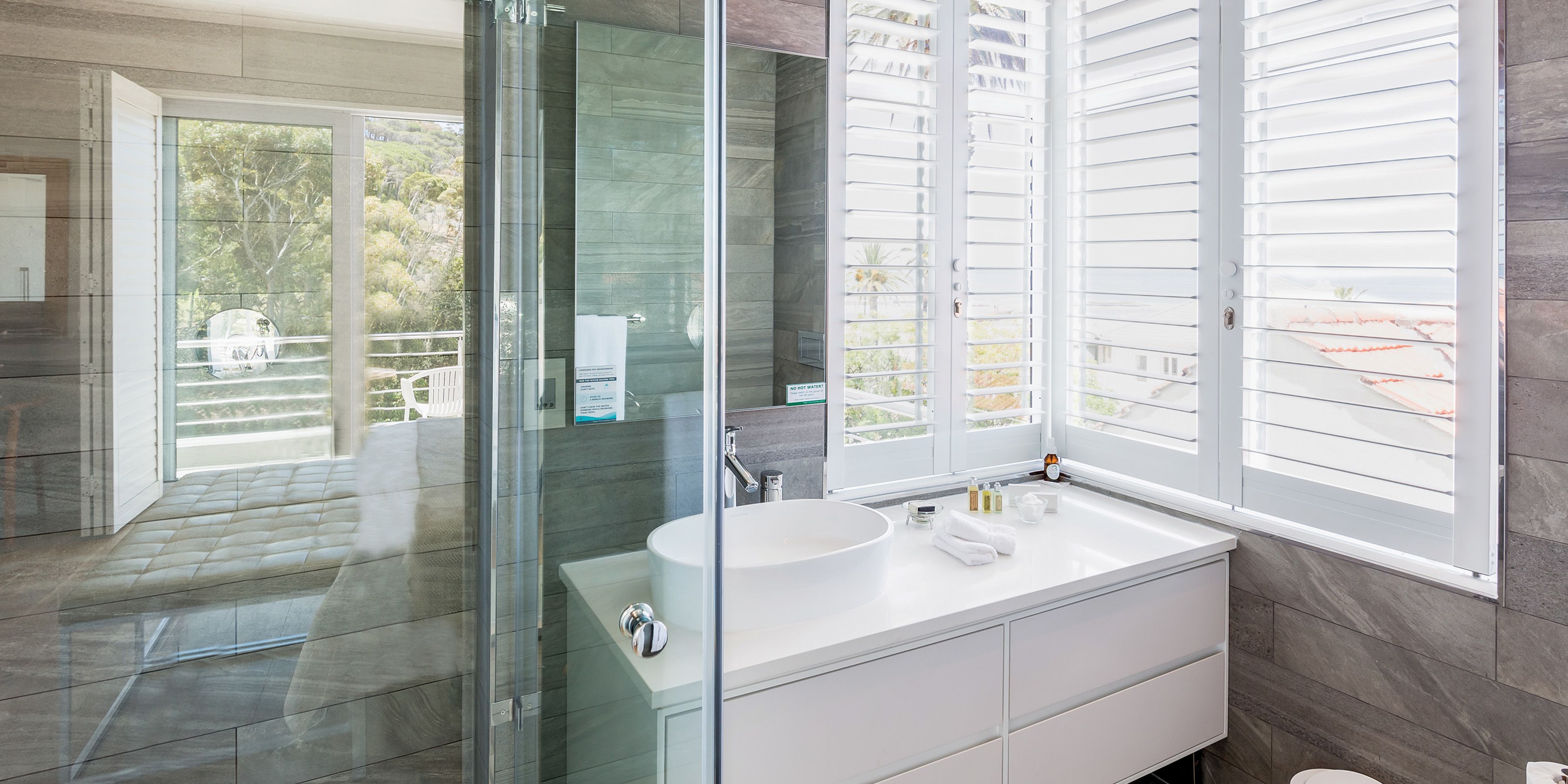 A modern bathroom with a glass shower enclosure, a large sink, and a window with blinds.