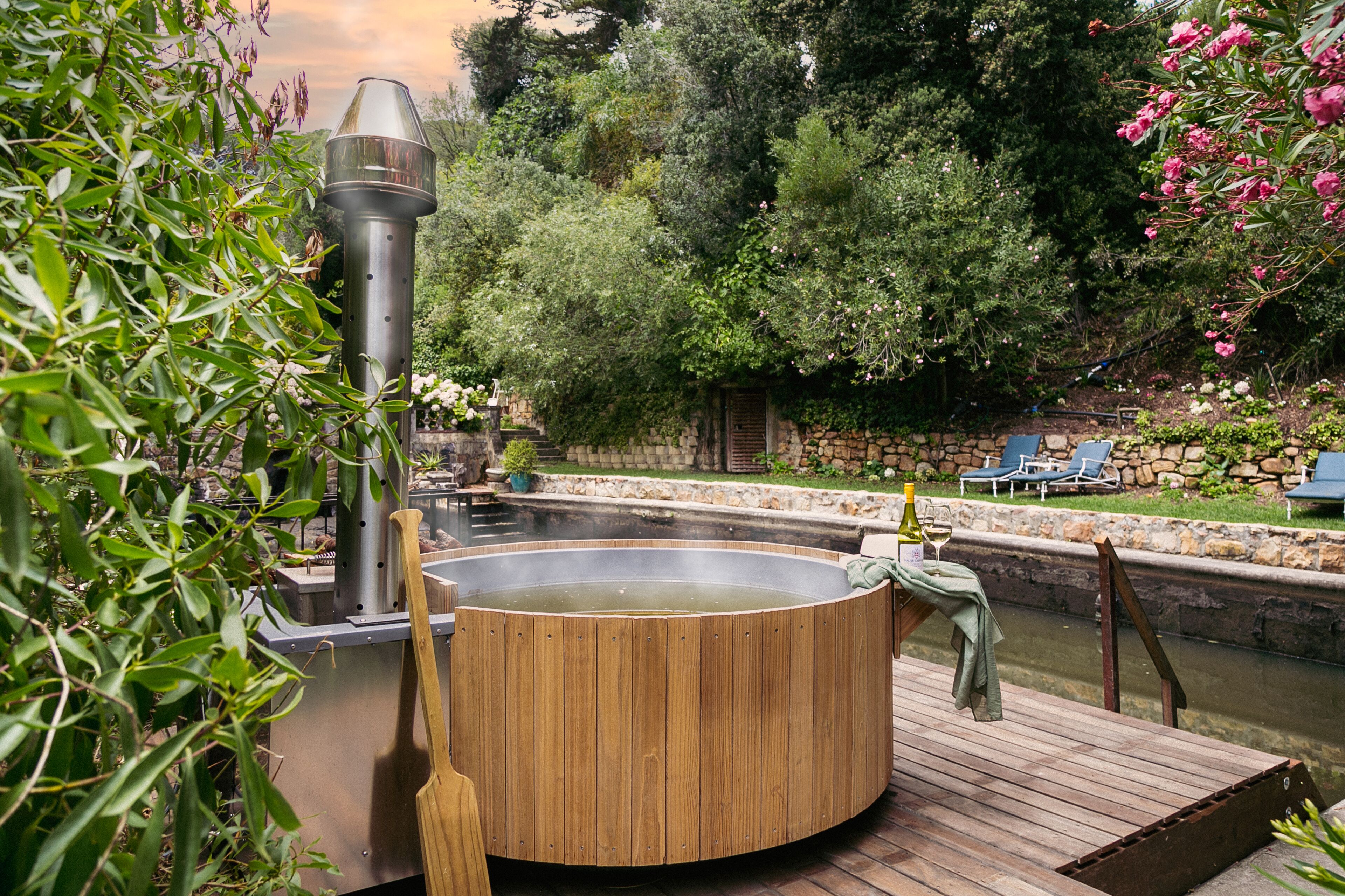 Ein Whirlpool, umgeben von viel Grün, einer Steinmauer und einem kleinen Pool.