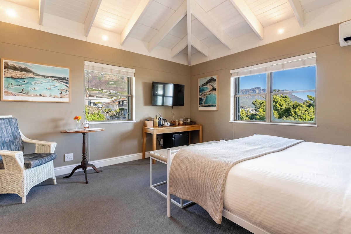 A bedroom with a bed, a chair, a desk, a TV, and large windows with scenic views.