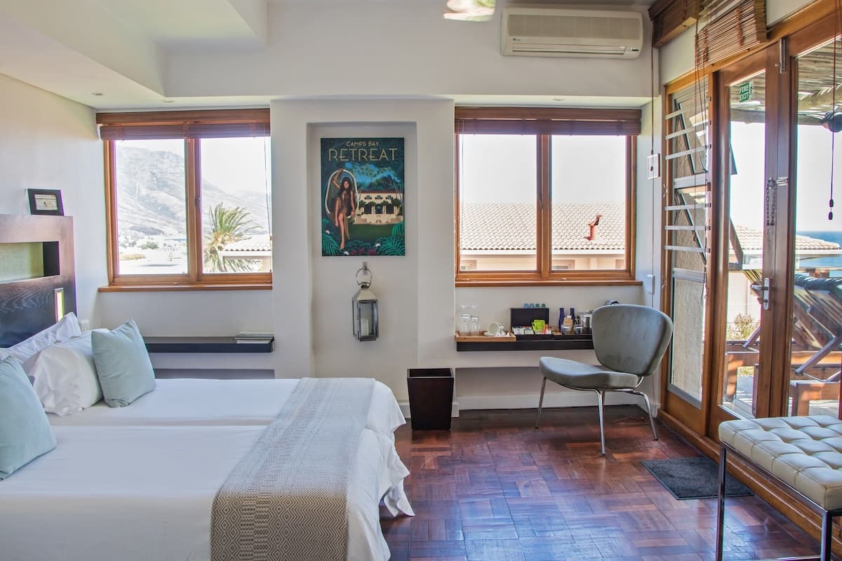 A hotel room with a bed, a desk, a chair, and large windows offering a view of the mountains.