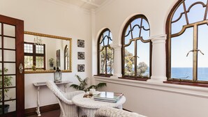 A room with white wicker furniture, a large mirror, and arched windows overlooking the sea.