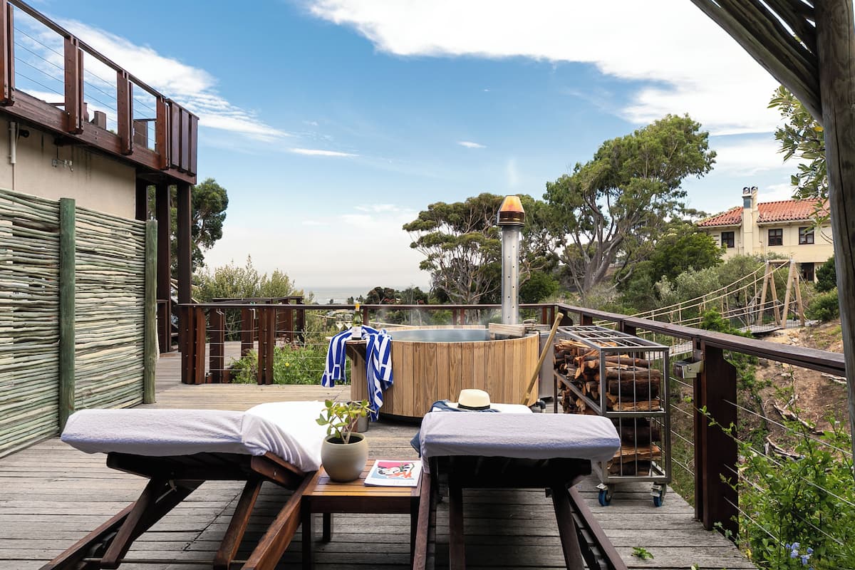 A wooden deck with two massage tables, a hot tub, and a cart with logs.