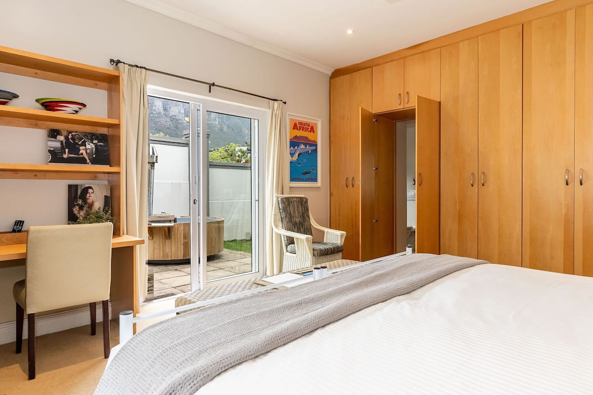 A bedroom with a large bed, a desk with a chair, a wardrobe, and a view of the outdoors through a sliding door.
