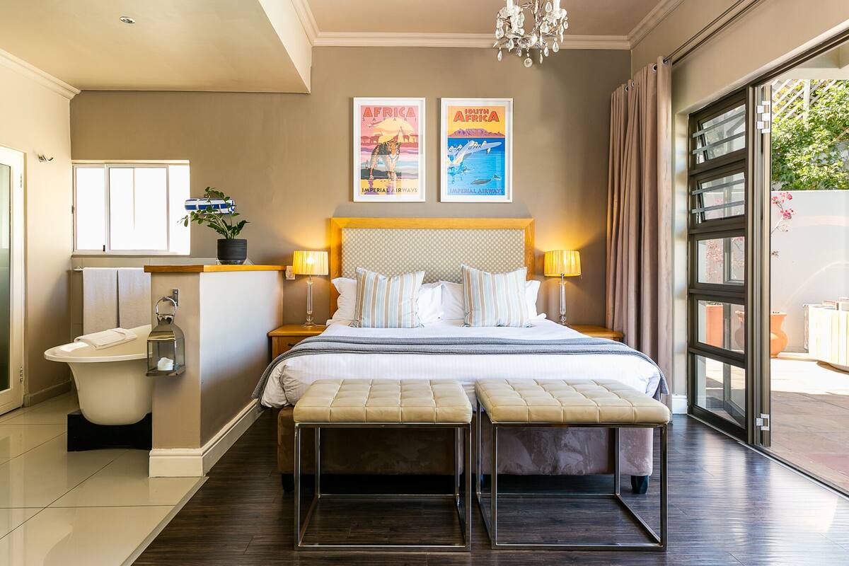 A hotel room with a large bed, two bedside lamps, a nightstand, a toilet, and a window with curtains.