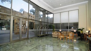 Un vestíbulo amplio con un muro de vidrio, una zona de estar con sofás y sillones, y un mostrador de recepción.