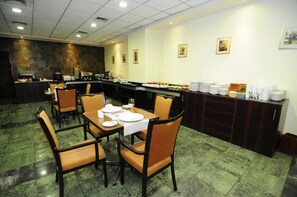 A restaurant with a buffet setup, including a counter with food items and a variety of plates and cups stacked on a shelf. - Diego De Almagro Calama (Calama)