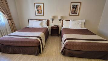 A hotel room with two beds, a nightstand, and a lamp.