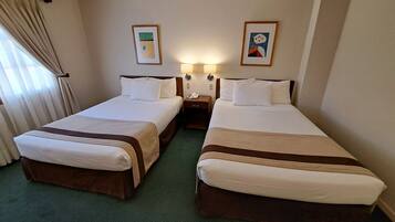 Una habitación de hotel con dos camas, una mesita de noche con un teléfono y dos lámparas fijadas a la pared.