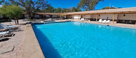 A clear blue swimming pool with lounge chairs and a covered area with tables and chairs.