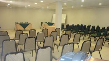 Un salón de conferencias con filas de sillas, mesas y una pizarra.